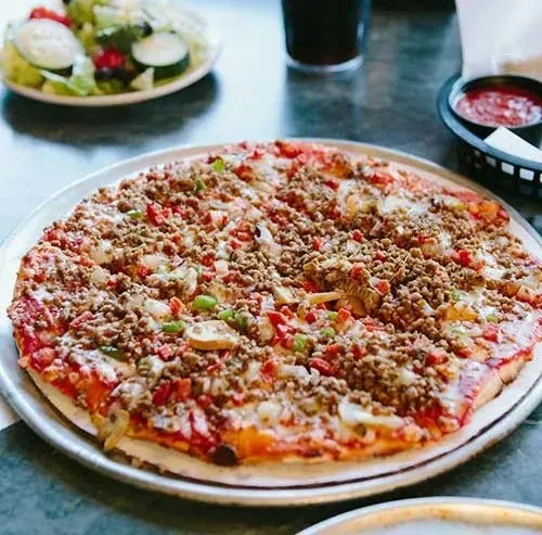 Close-up of a meat and vegetable pizza with salad and sauce.