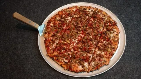 Sliced pizza with meat and red toppings on a metal pan.