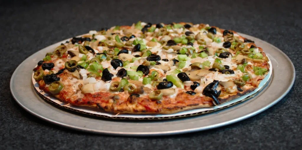 Whole pizza with bell peppers, olives, mushrooms, onions on metal pan.