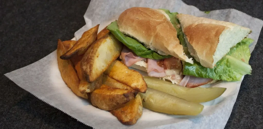 Ham sandwich halves, golden potato wedges, and two dill pickles.