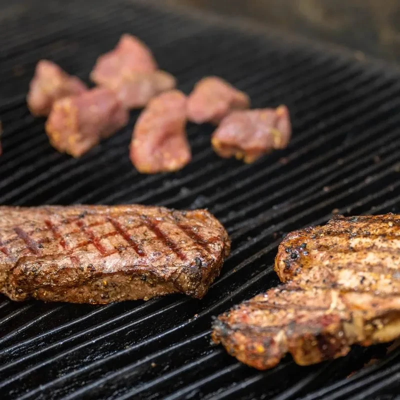 Steaks and other meat cooking on a dark, ridged grill.