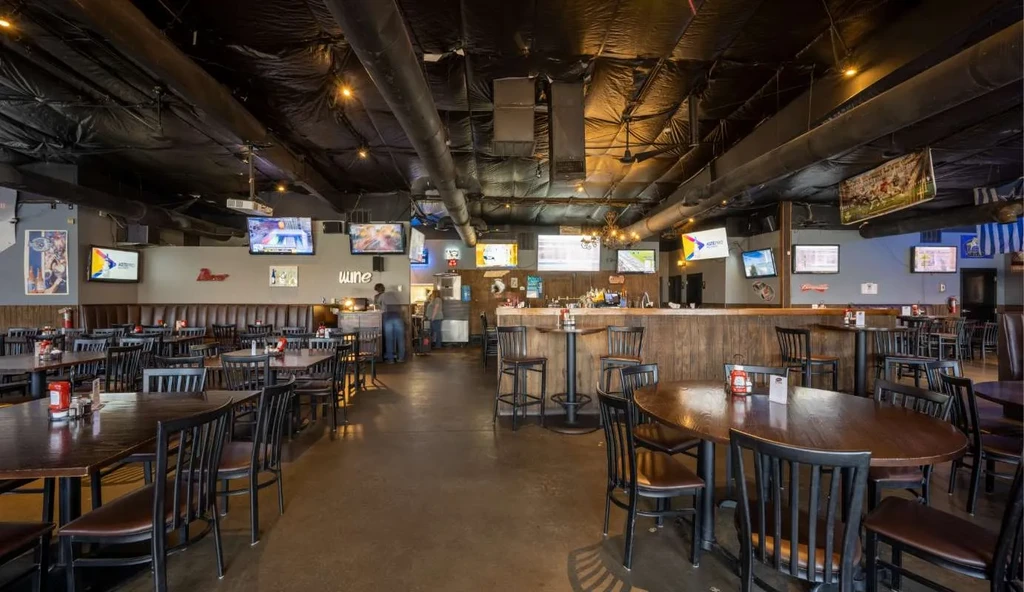 Spacious sports bar with dining tables, prominent bar, and multiple TVs.