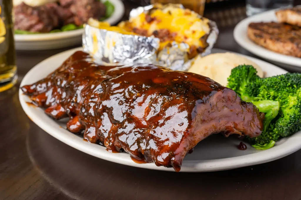 Full rack of glossy barbecued ribs with broccoli and mashed potatoes.