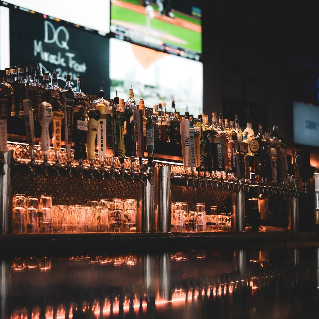 Warmly lit bar counter displaying many beer taps and liquor bottles.