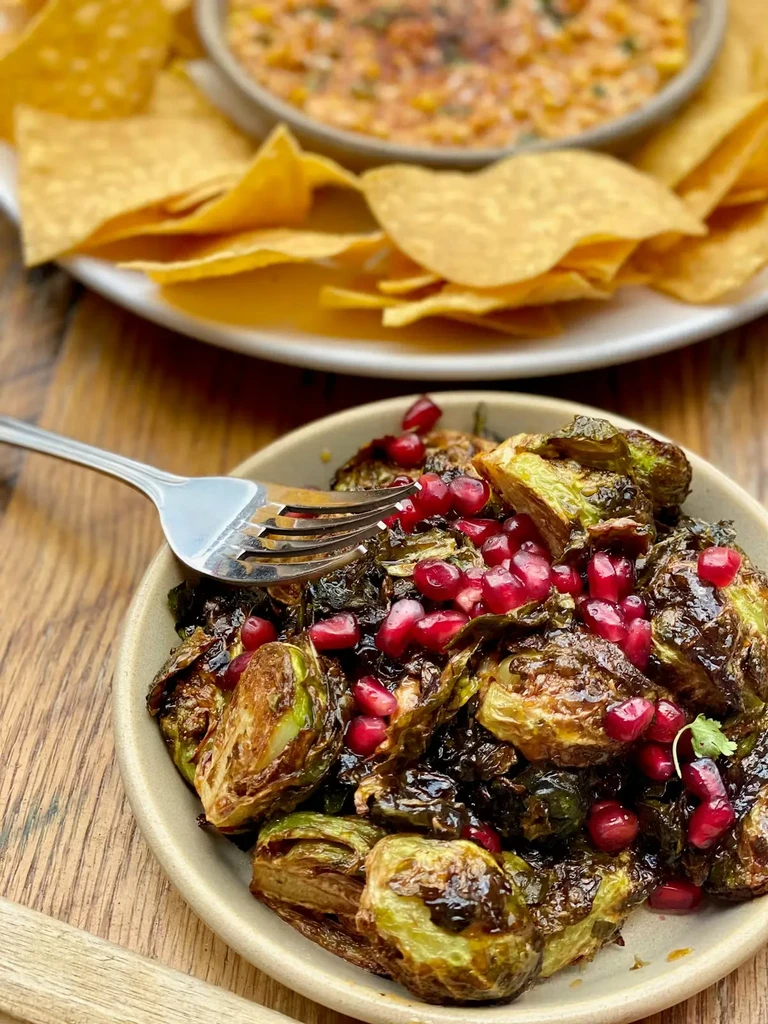 Roasted Brussels sprouts with pomegranate, tortilla chips, and dip on rustic wood.