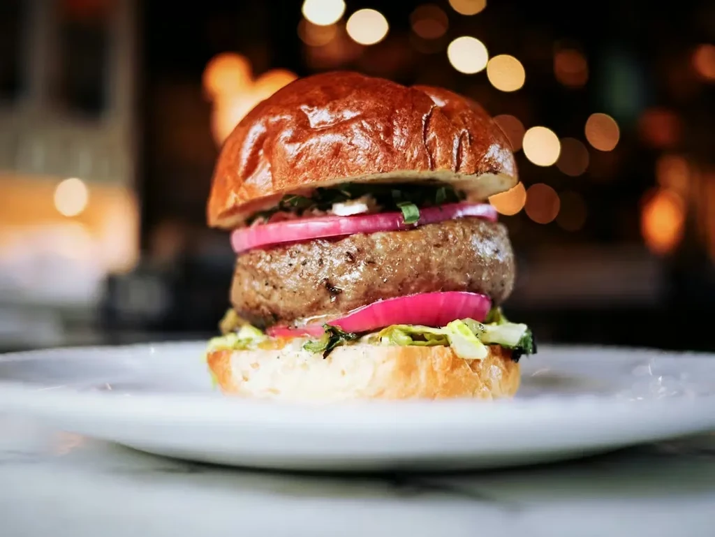 Close-up gourmet burger with brioche bun, patty, pickled onions, and lettuce.