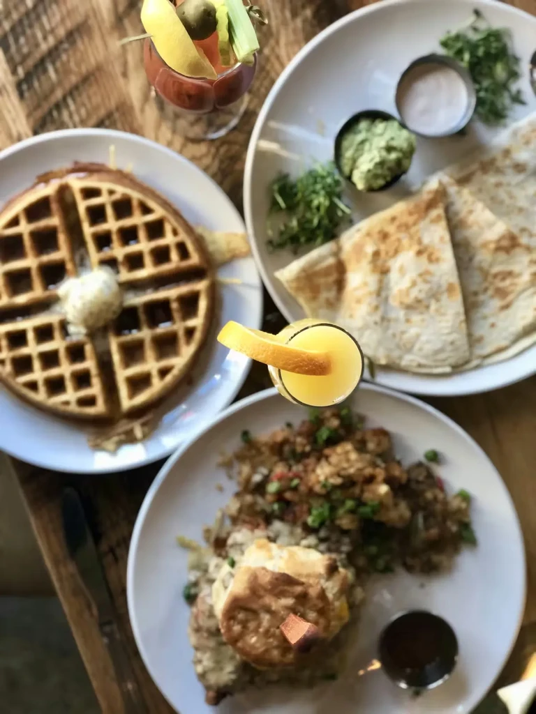 Overhead: rustic table with waffle, flatbreads, eggs, Bloody Mary, mimosa.