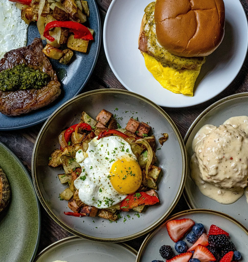 Flat-lay of multiple breakfast and brunch dishes on a dark wooden table.