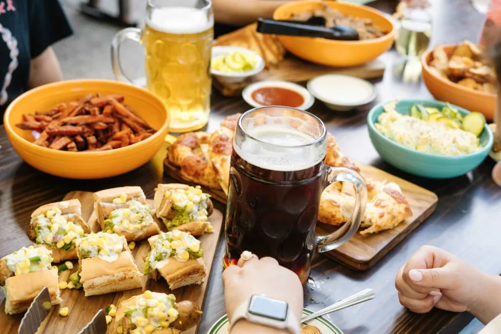 Hand holds dark beer stein among sliders, fries, and diverse food.