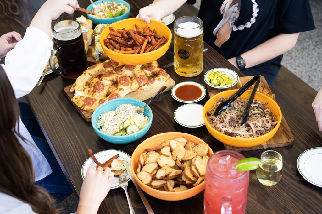 Overhead view of a dining table with diverse food, drinks, and hands.