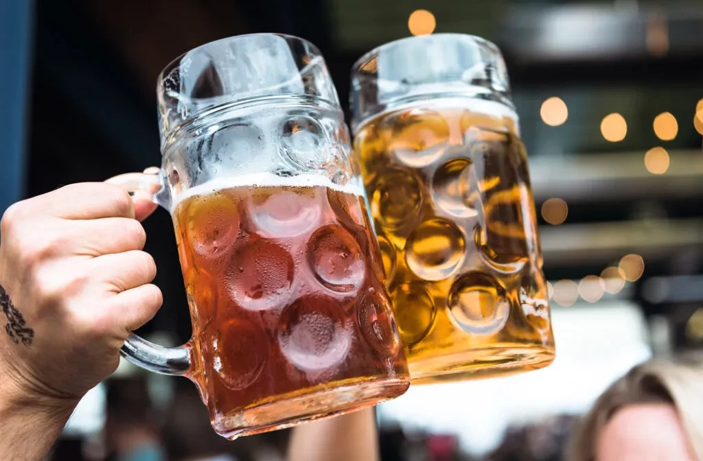 Two cold beer mugs, different beers, clinking in a toast.