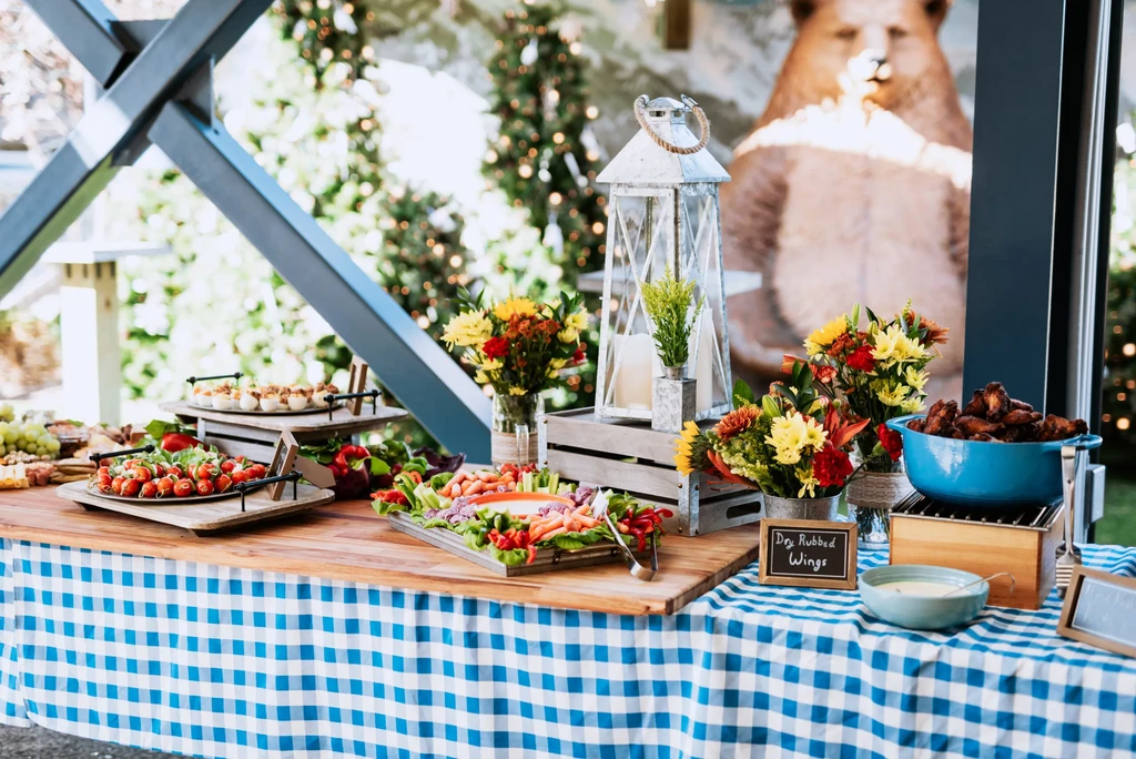 A festive outdoor buffet table with dry-rubbed wings, vegetables, and flowers.