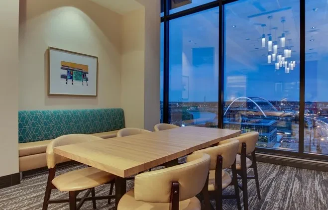Modern dining area with long table, teal booth, and city skyline view.