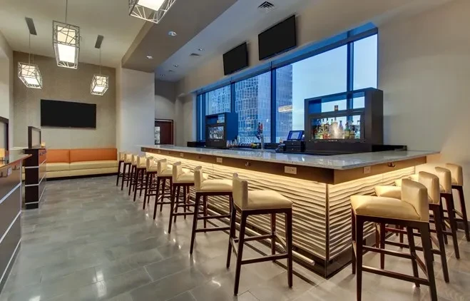 Empty modern bar with illuminated counter, city view, and banquette seating.