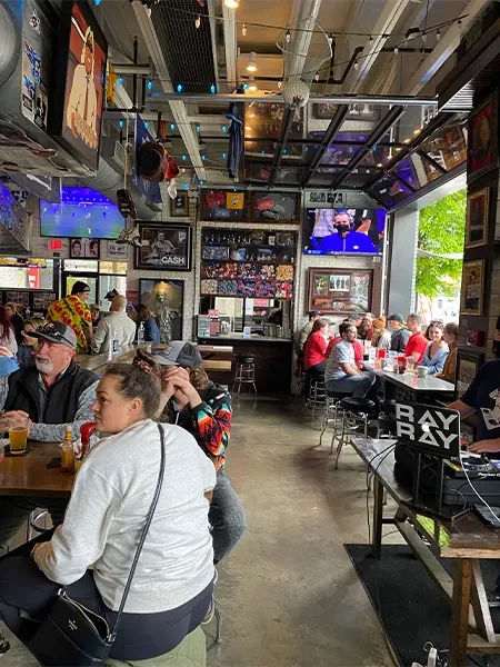 Lively restaurant interior with patrons, sports TVs, DJ, and open windows.