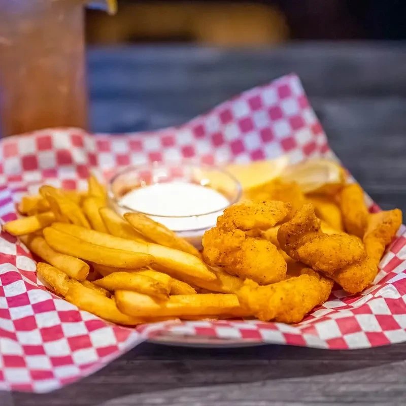 Tray of golden french fries, fried pieces, dipping sauce, and lemon.
