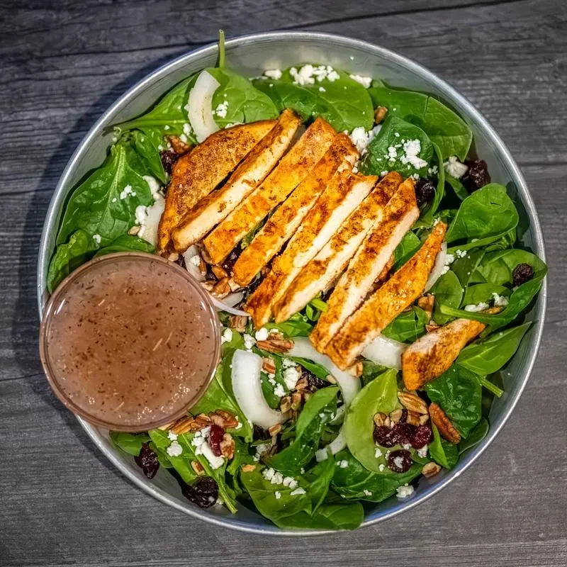 Spinach salad with grilled chicken, crumbled cheese, cranberries, and nuts.