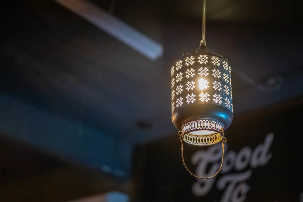 Cylindrical dark metal pendant light, ornate cut-outs glow warmly.