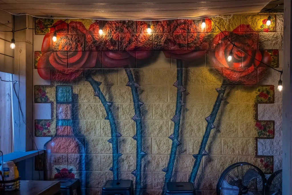 Vibrant red rose mural on a brick wall, lit by Edison bulbs.