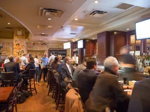 A bustling bar with patrons, blurred bartender, TVs, and bottles.