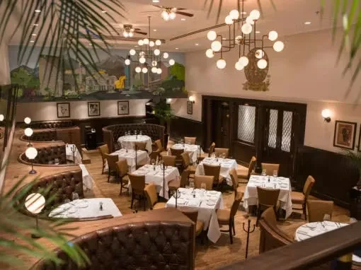 Elegant restaurant interior with tables, booths, warm lighting, and a landscape mural.