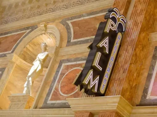 Vertical "THE PALM RESTAURANT" sign next to a classical statue in marble hall.