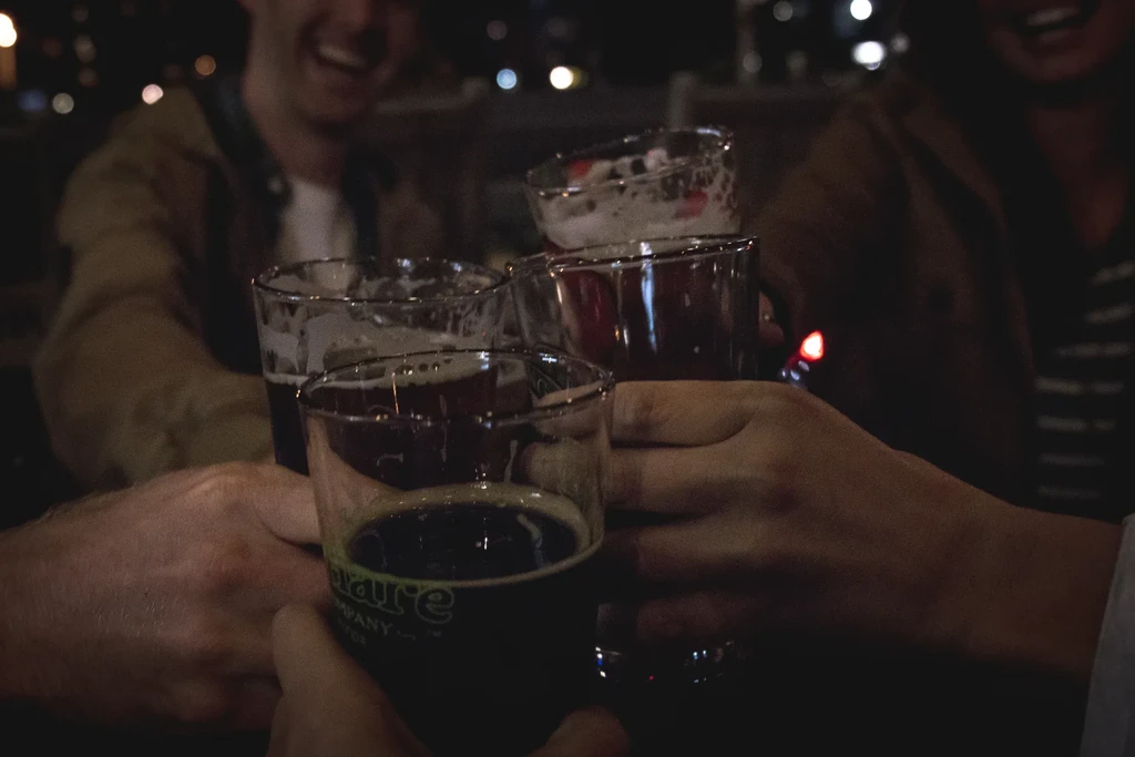Four hands clinking dark drinks in a dimly lit setting.