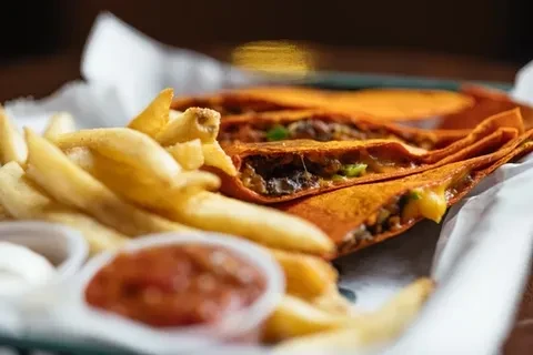 Golden-brown french fries, orange tacos, and two dips on a tray.