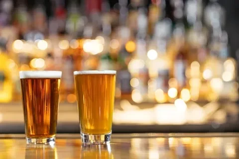 Two glasses of beer on a reflective bar counter, blurred background.