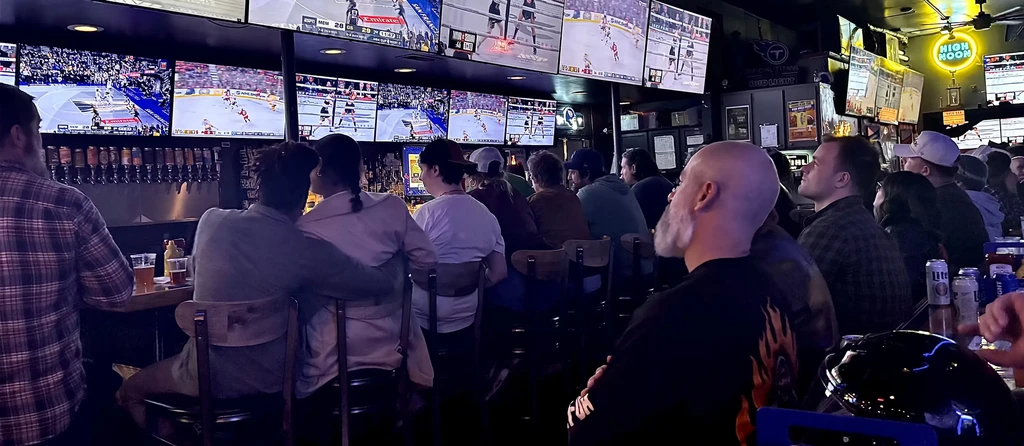 Dimly lit sports pub interior, patrons watching multiple sports on TVs.