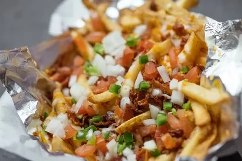 Golden-brown loaded fries topped with bacon, cheese, tomatoes, onions, and peppers.