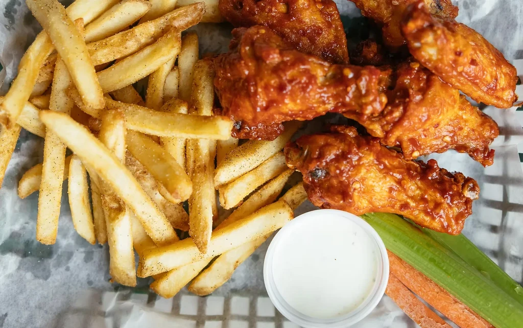 A basket of sauced chicken wings, French fries, dipping sauce, and veggies.