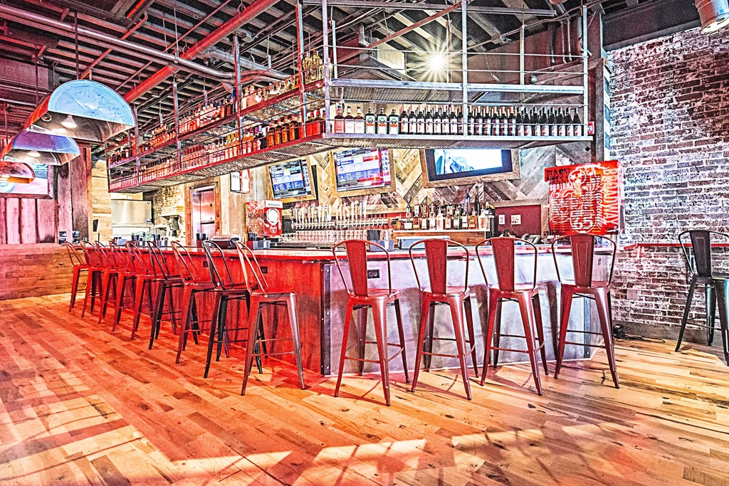 Modern industrial bar interior with red stools, stocked shelves, and TVs.