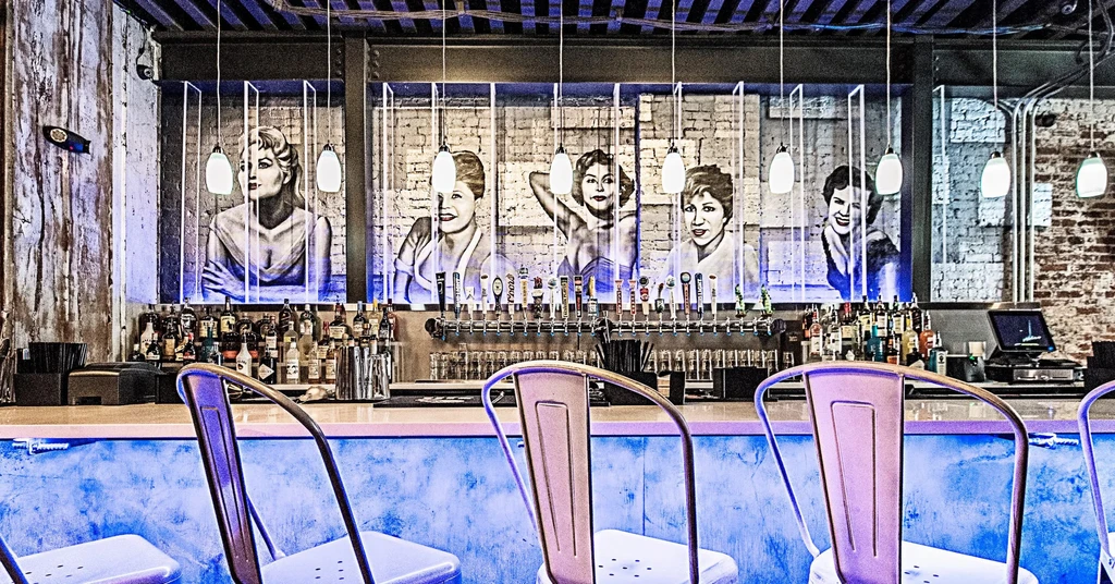 Blue-purple lit bar with beer taps and five women's artworks.