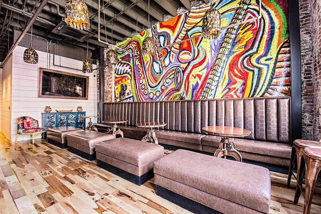 Restaurant interior with a large colorful mural and industrial-chic decor.