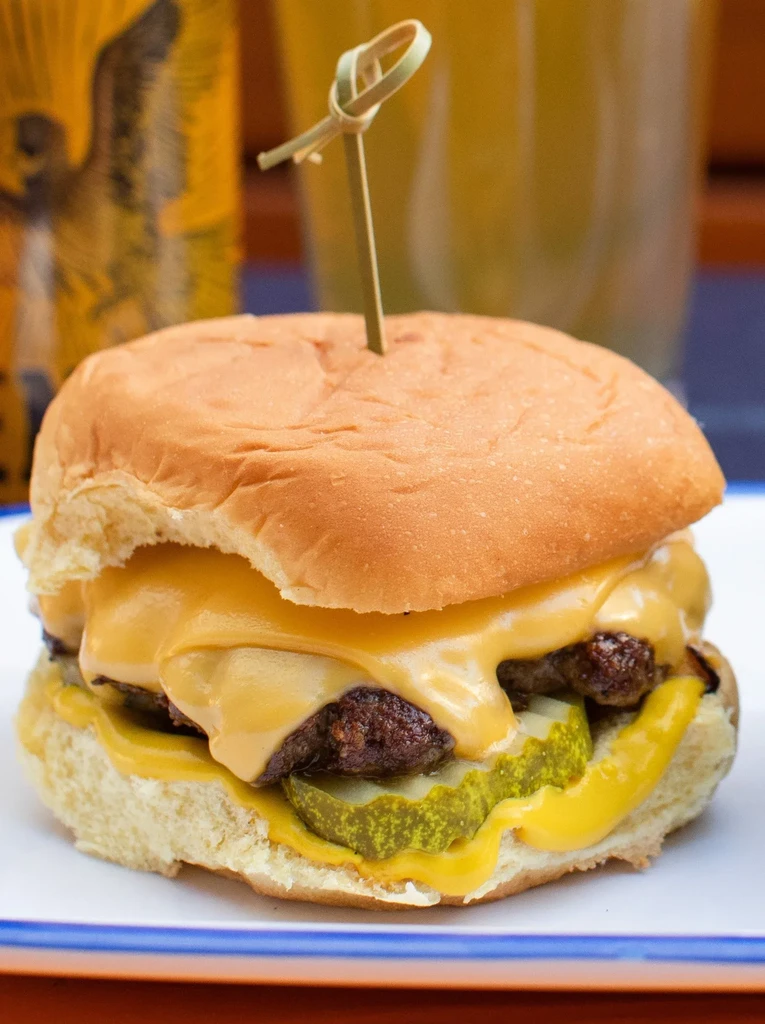 Close-up of a double cheeseburger with melted cheese, pickles, and a wooden skewer.