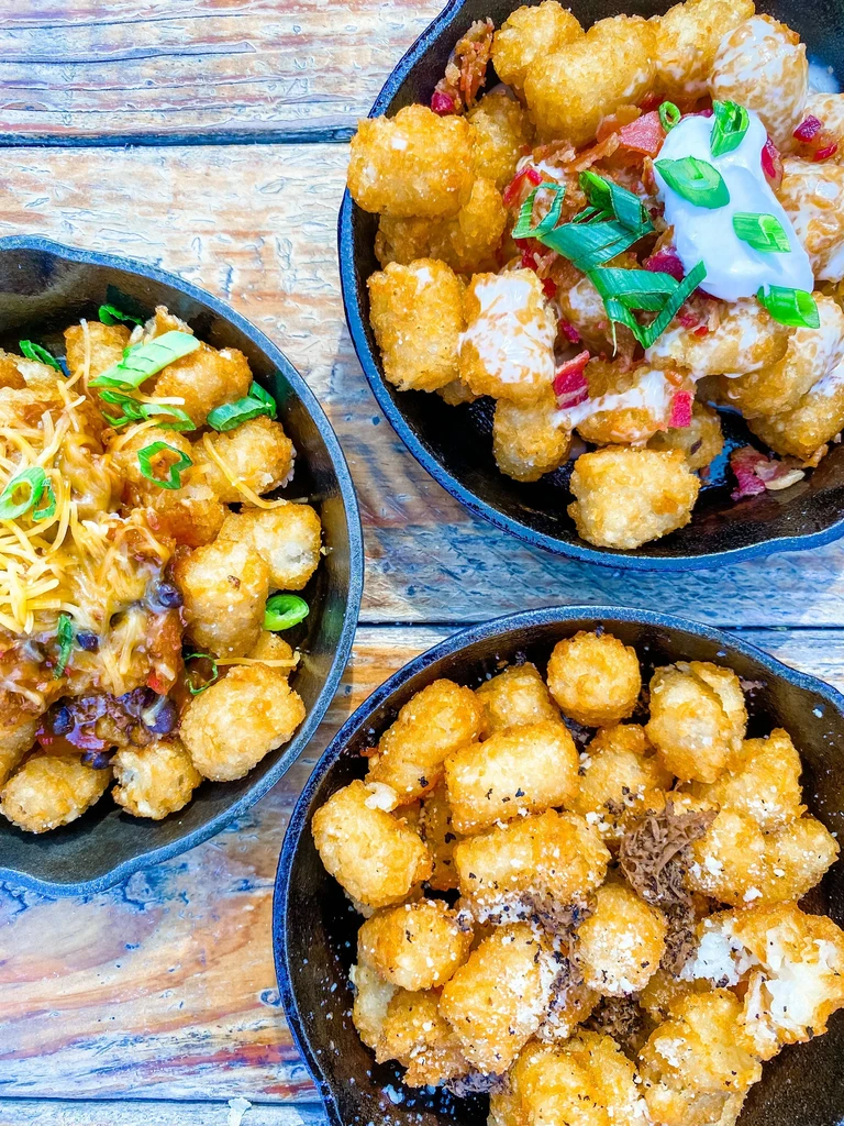 Three skillets of crispy tater tots with different savory toppings.
