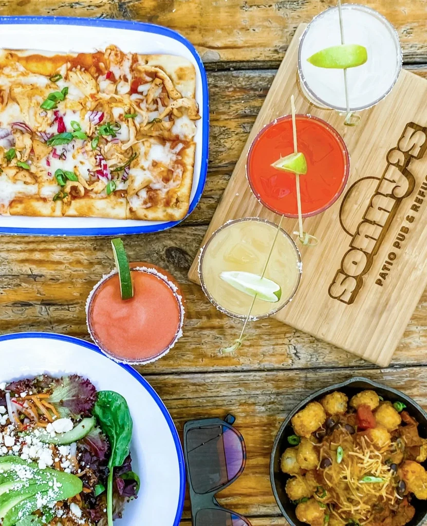 Overhead view of a wooden table with pizza, cocktails, salad, and skillet.