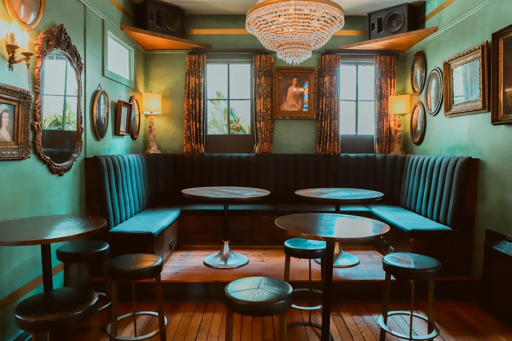 Ornate restaurant with dark teal booth, wood tables, mirrors, chandelier.