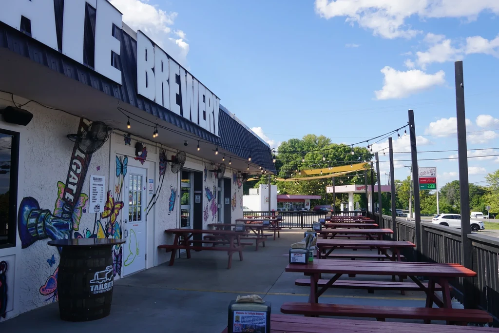 Tailgate Brewery exterior with colorful mural, picnic tables, and string lights.