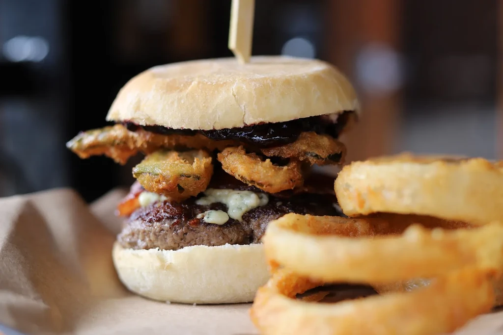 Close-up of a gourmet stacked burger with onion rings on parchment paper.
