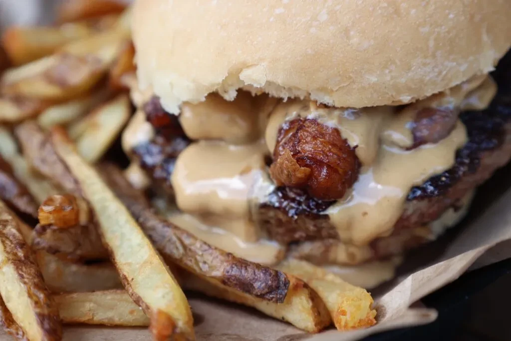 Large burger with creamy sauce, crispy bits, and rustic fries.