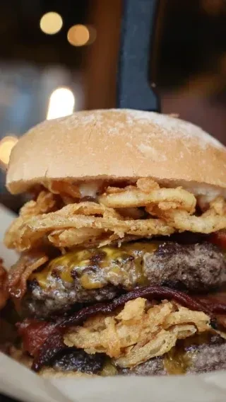 Tall burger with patties, cheese, bacon, and onion rings, held by a knife.
