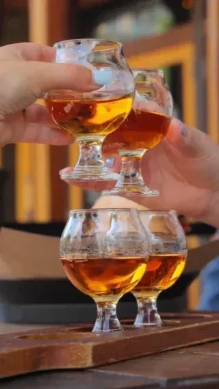 Hands lift two amber spirit glasses, two more on a paddle.