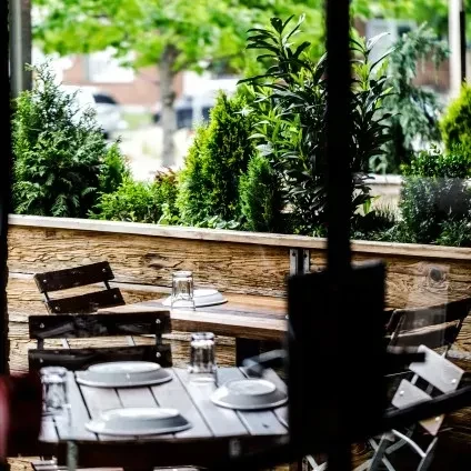 Rustic outdoor patio with two set wooden tables, lush foliage.