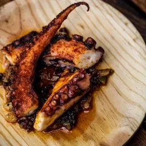 Grilled octopus tentacles on a wooden plate with a dark sauce.