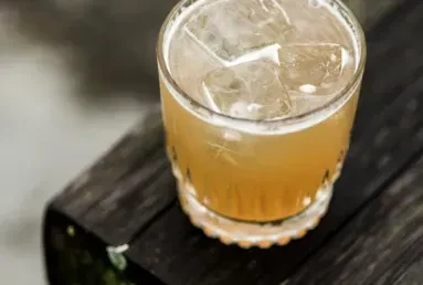 Textured glass with amber iced drink and condensation on rustic wood.