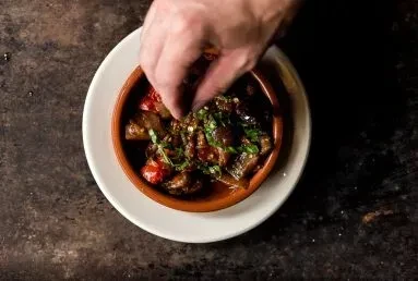 Hand garnishing rustic vegetable stew with fresh herbs in a bowl.