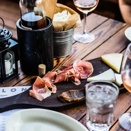 Rustic wooden table with meat, cheese, bread, wine, and candle.
