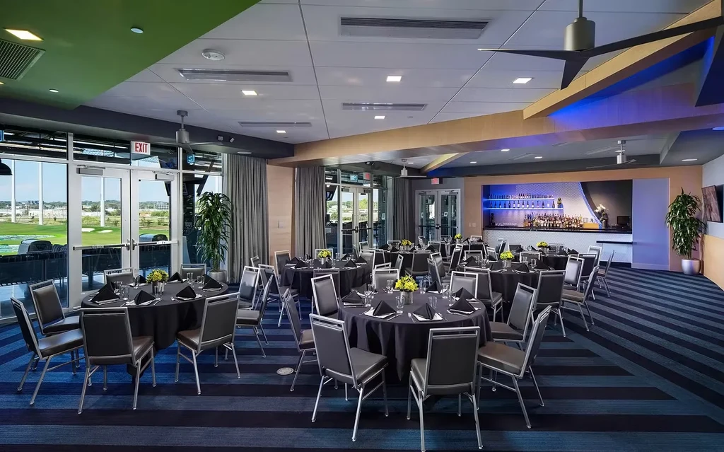 Spacious, modern event room with banquet tables, bar, and golf view.
